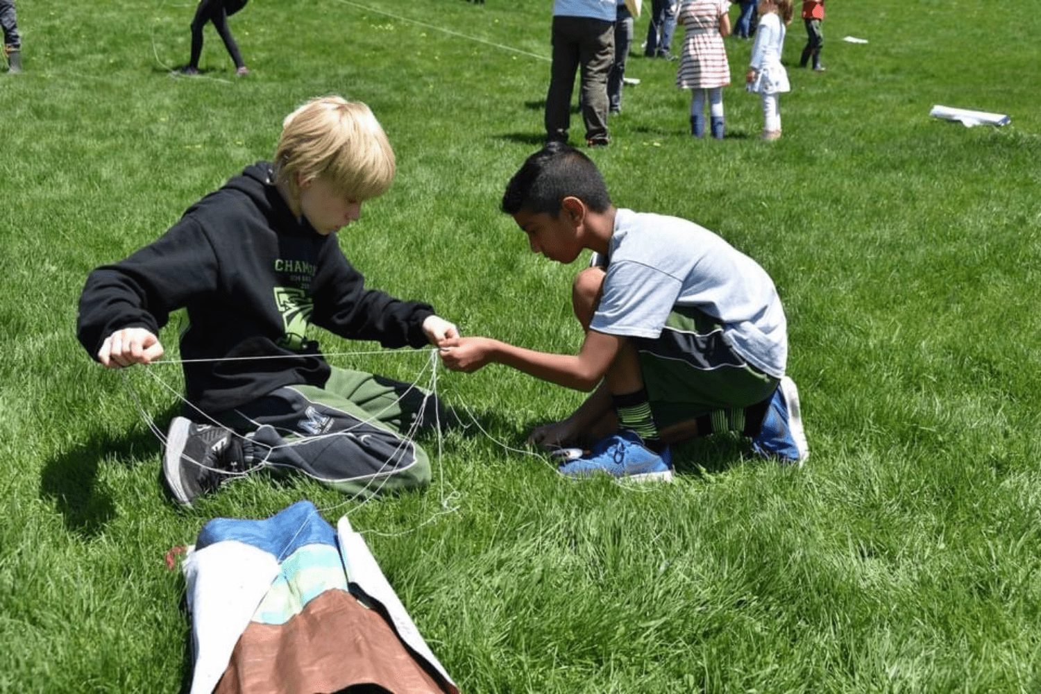 Two children on the grass untangling kite lines.